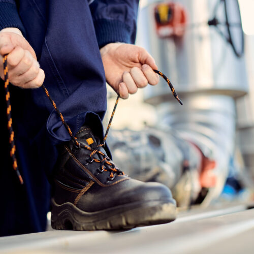 Unrecognizable construction worker tying his shoelace outdoors.